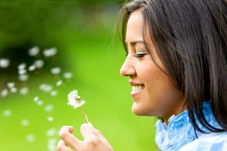 Mujer hermosa soplando una flor y sonriendo